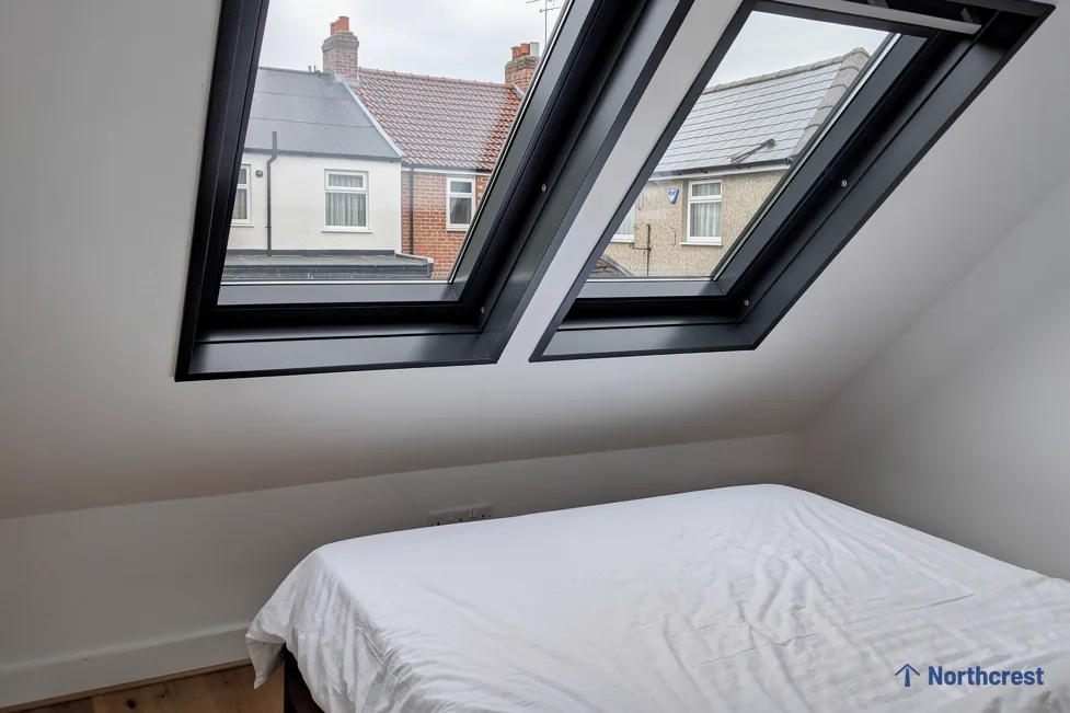 Loft bedroom with two black-framed roof windows side by side above a made bed