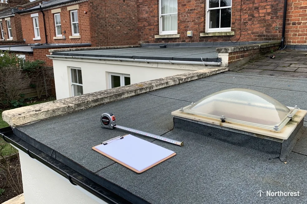 Old dome rooflight on a felt flat roof with a tape measure and blank clipboard