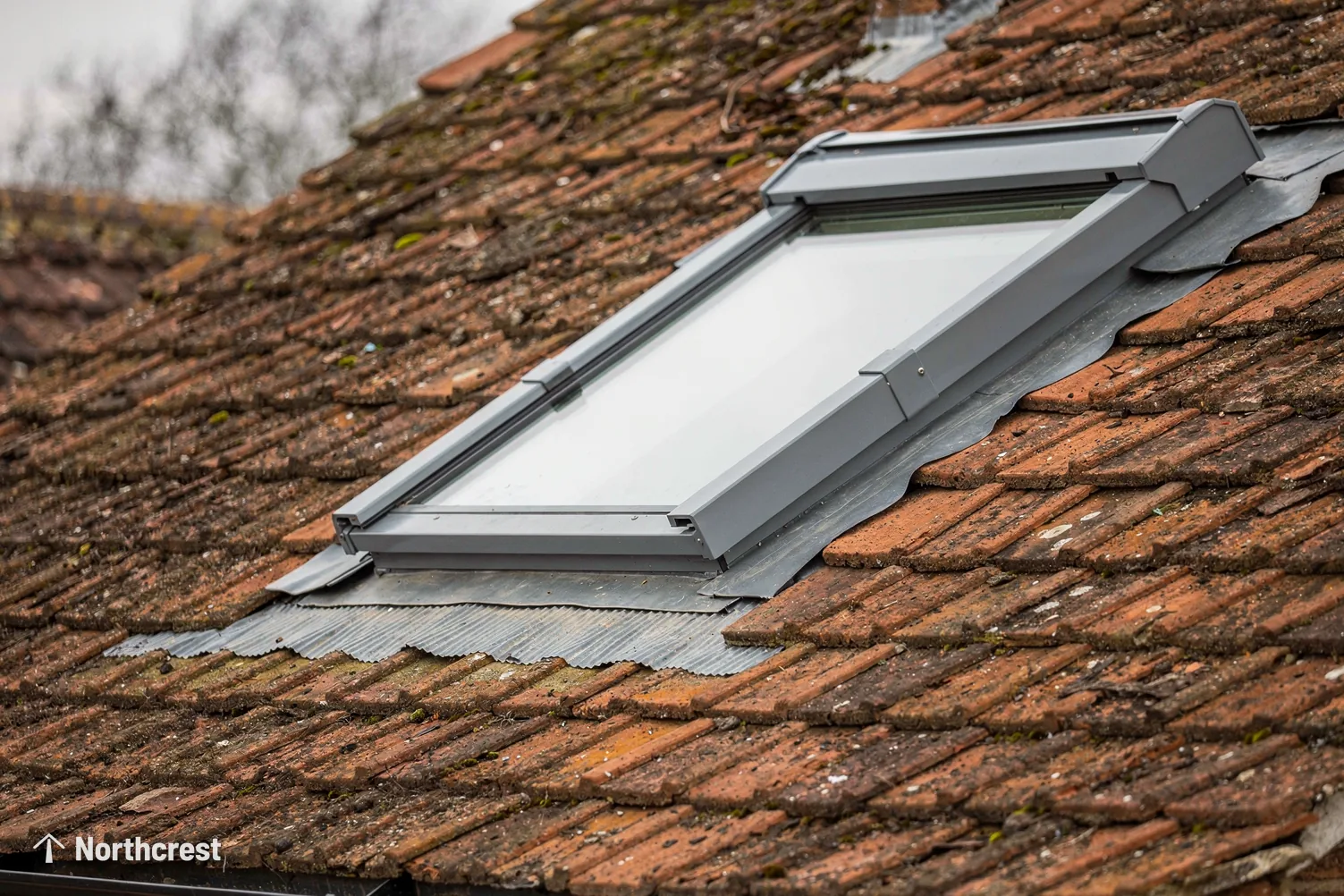 Grey aluminium roof window with its flashing set neatly into weathered clay roof tiles