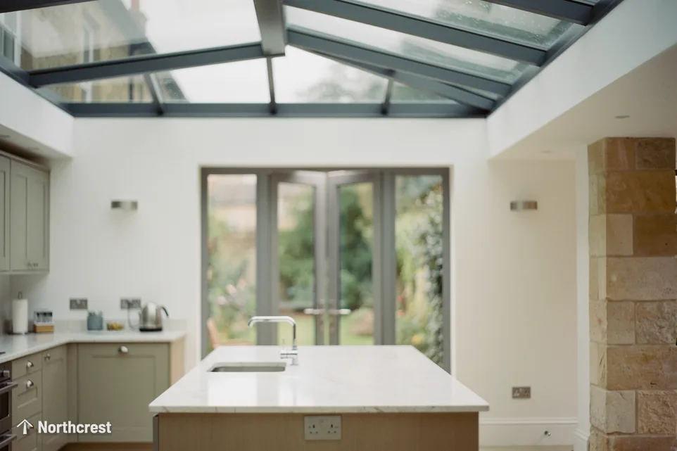 Kitchen with a marble island and French doors under a glazed roof with grey glazing bars