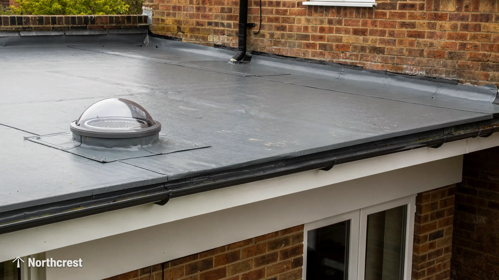 Clear sun tunnel dome on a grey flat roof of a brick extension