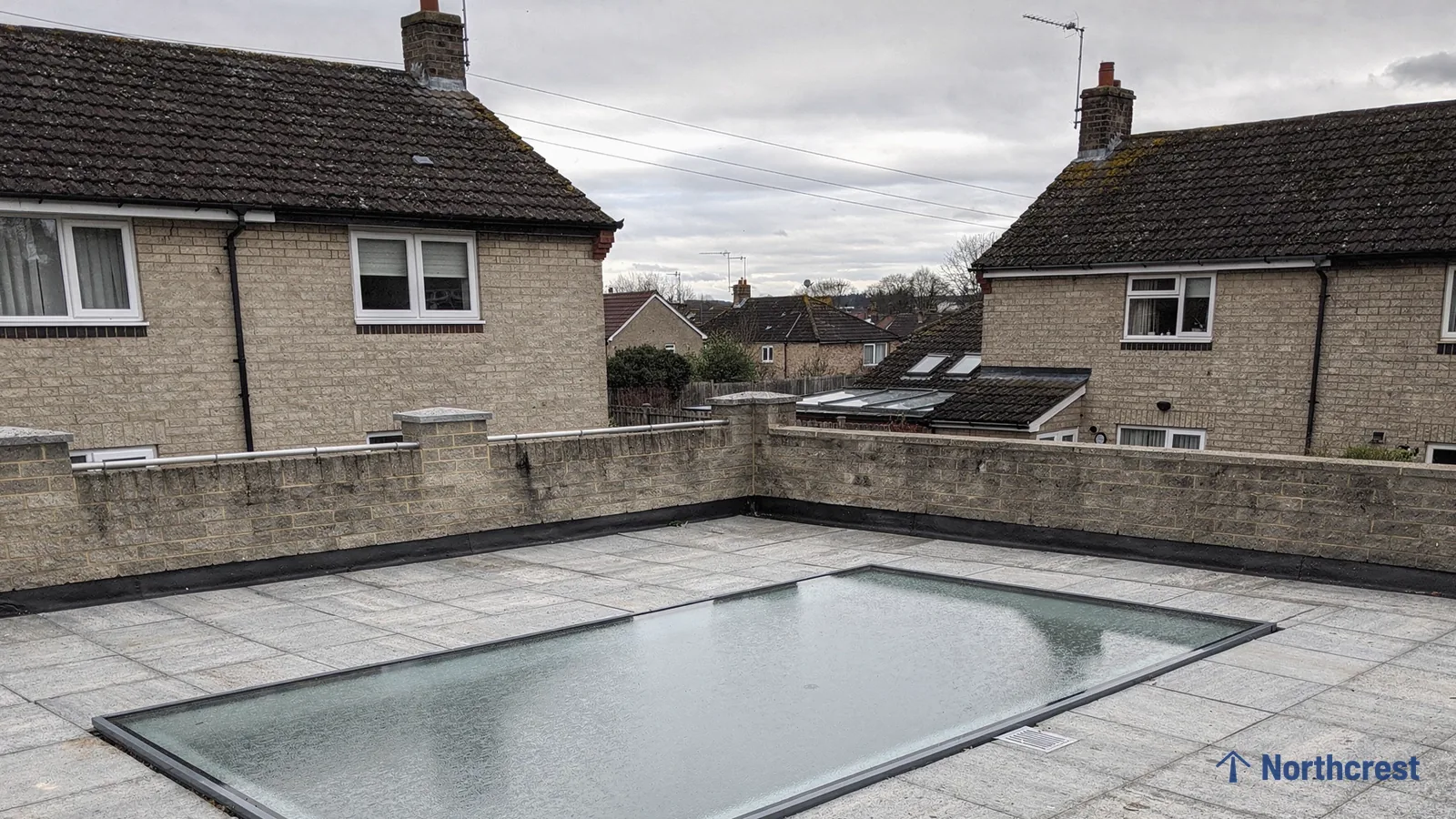 Walk-on rooflight set flush into pale grey paving on a roof terrace with a stone parapet